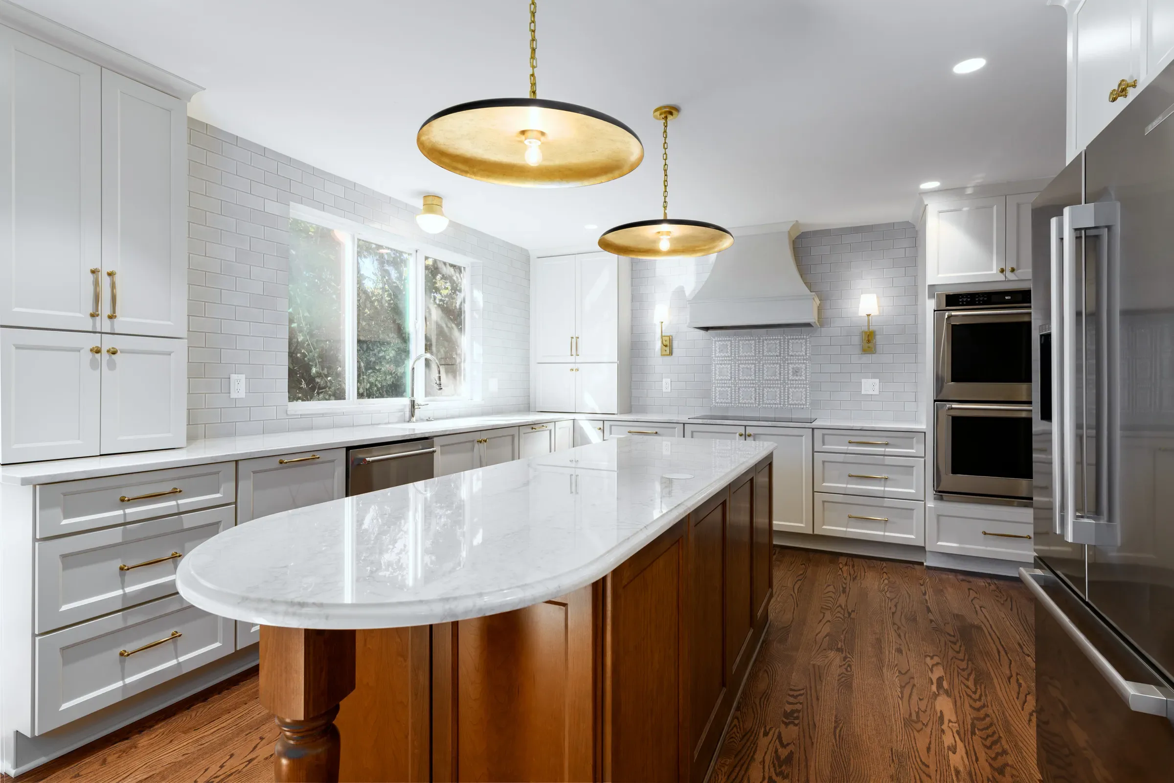 Remodeled white kitchen with a marble waterfall island, brass pendant lights, and double wall ovens
