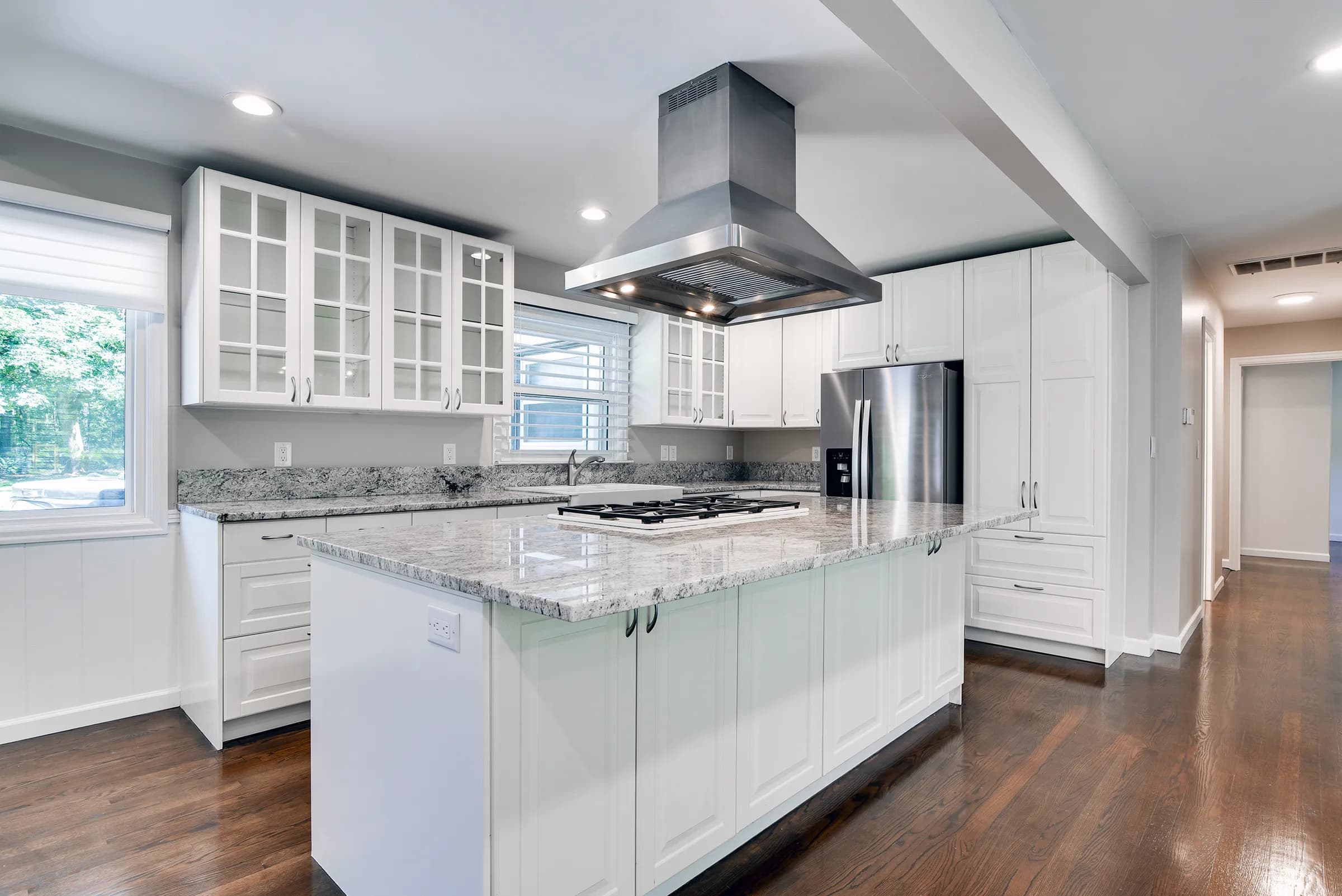 White kitchen remodel with a marble-topped island and stainless range hood