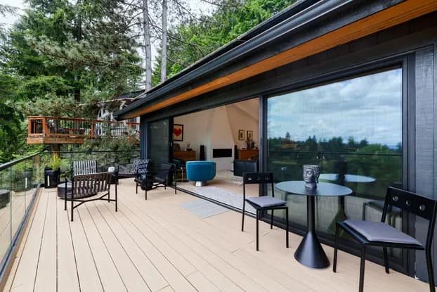 After photo of the completed West Hills double deck expansion showing the upper entertainment area with composite decking, glass railings, and Portland hillside views by Tortoise Construction LLC