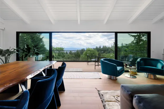 Remodeled West Hills living and dining room with a wall of black-framed glass opening onto the deck, glass railings and the Portland hillside view, by Tortoise Construction LLC
