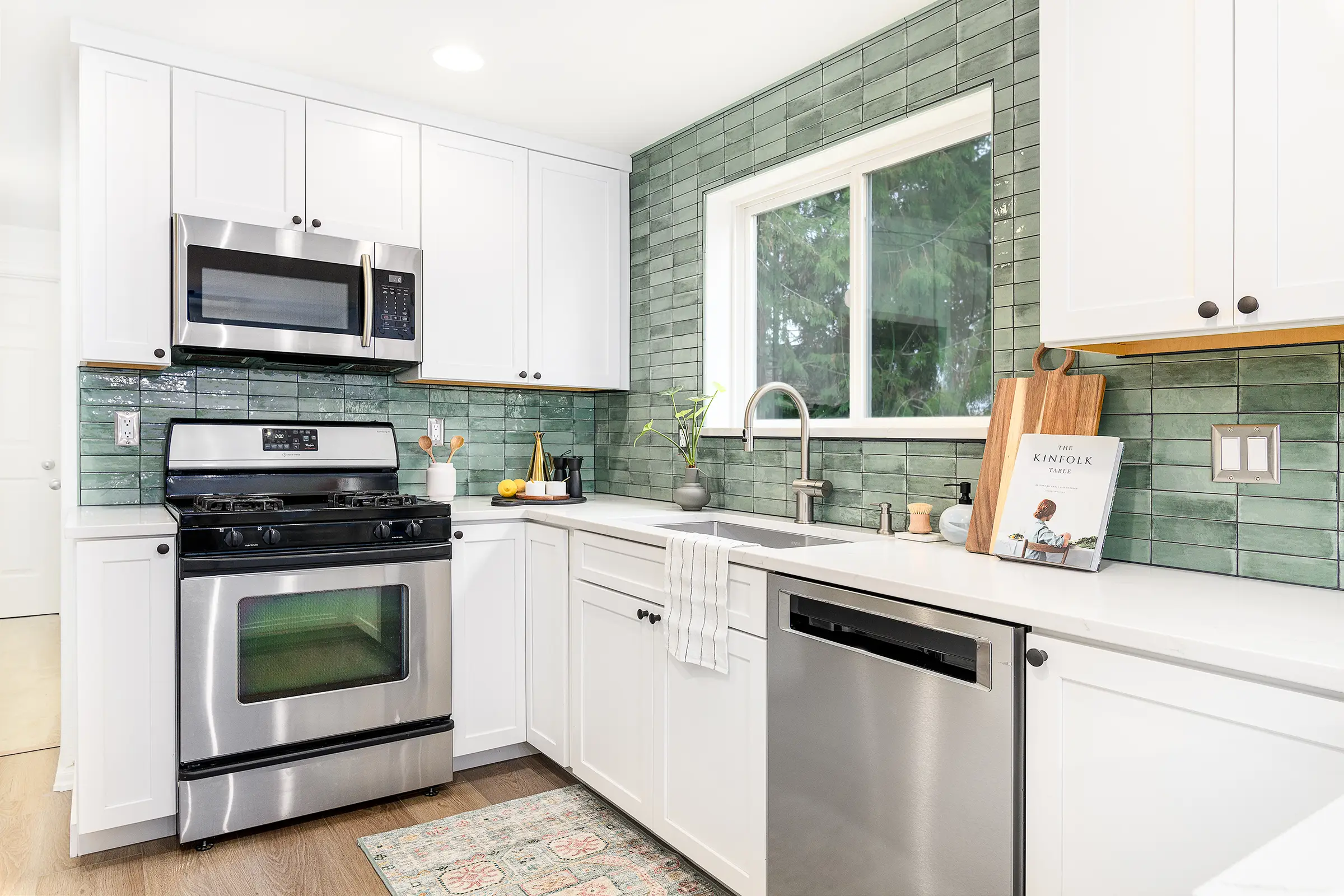 After photo of the renovated SE Portland kitchen at 6811 Mitchell Court showing white shaker cabinets, bold teal tile backsplash, quartz countertops, and luxury vinyl plank flooring by Tortoise Construction LLC