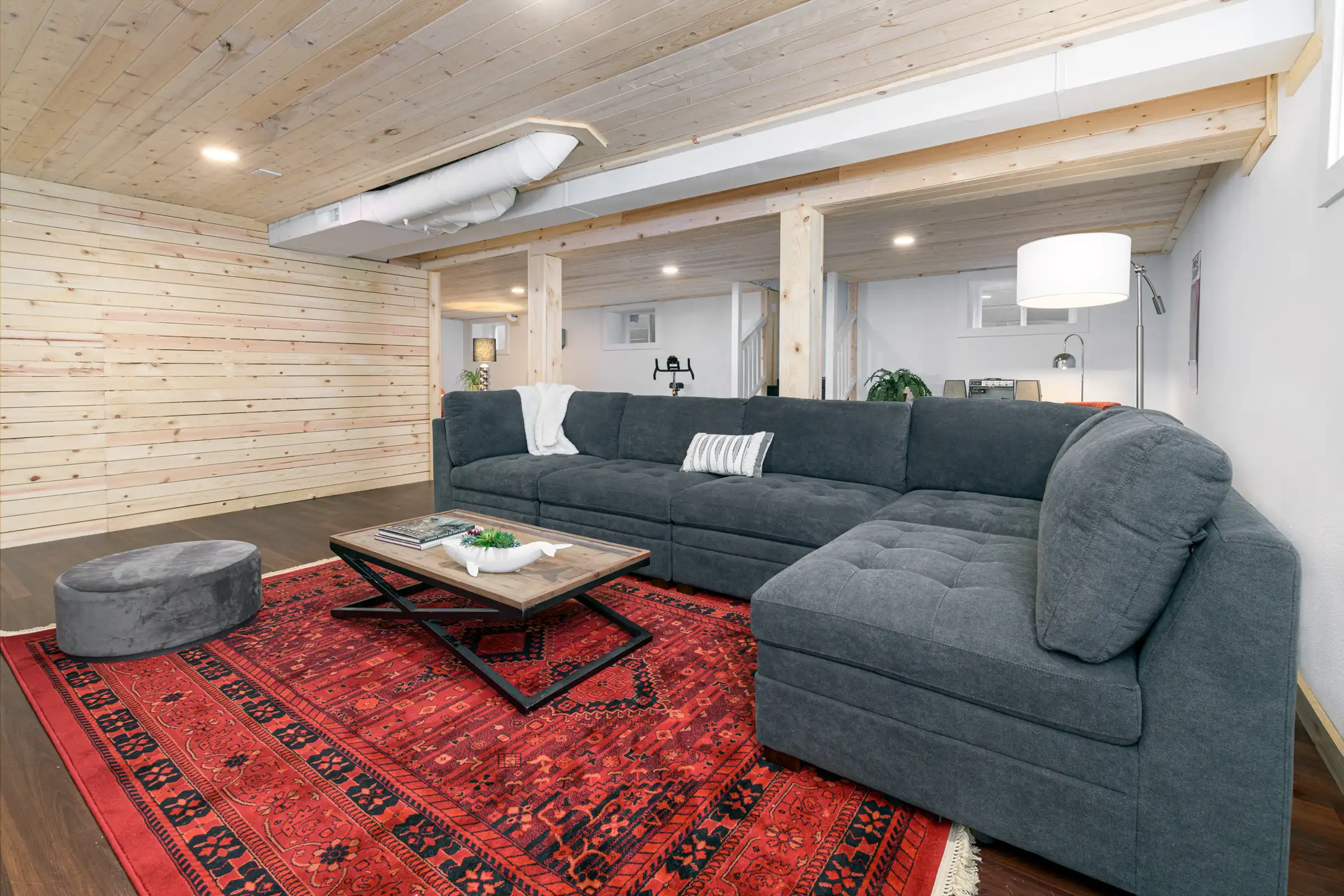 After photo of the finished SE Portland basement remodel at 23rd Ave showing the lounge area with recessed lighting, light wood ceiling detail, and modern durable flooring by Tortoise Construction LLC